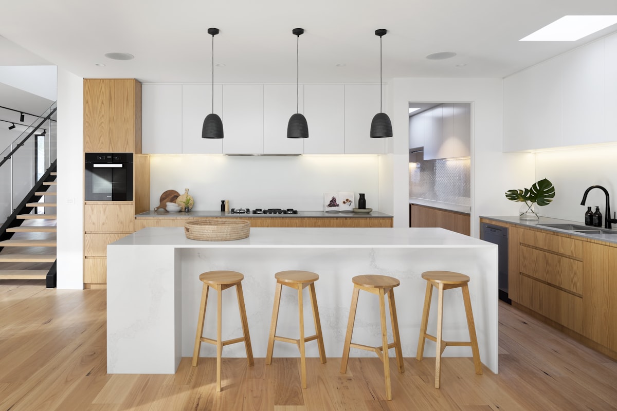 Warm open-plan kitchen and dining room with timber cabinetry, a white island, pendant lighting and timber stools